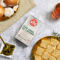 A box of Foie Gras De Canard with Cornichons on the side, spices and Liver spread toasts.