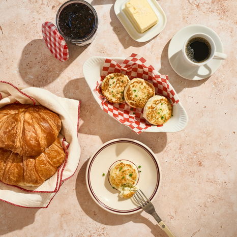 Breakfast setting with croissants, coffee, and Egg Bites on a checkered tablecloth.