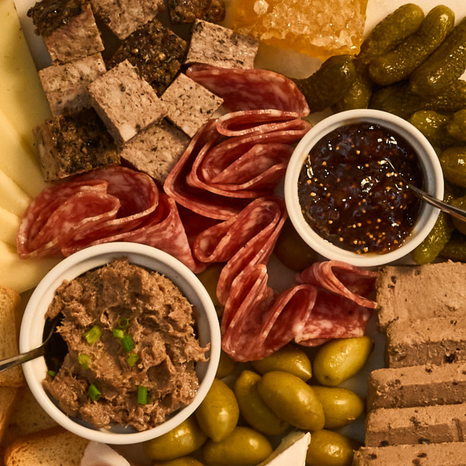 Platter with cured meats, olives, and dips on a wooden board