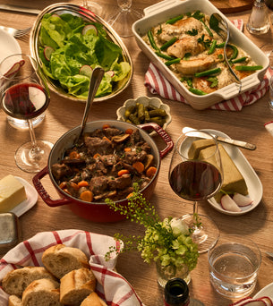Dining table set with various dishes including a pot of stew, bread, salad, and wine glasses.