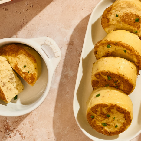 Egg Bites with green herbs on a white plate and bowl against a pink background