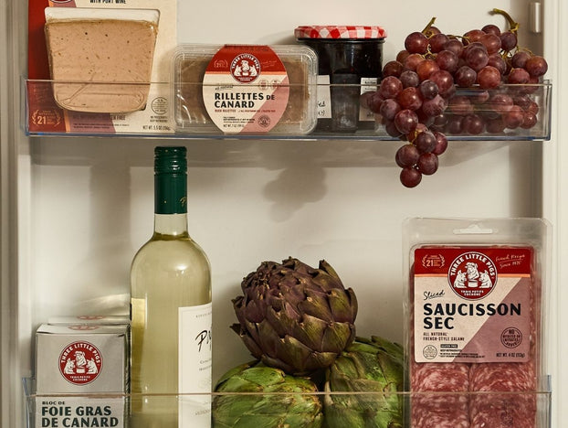 Shelf with various food items including a bottle of wine, artichokes, and packaged meats.